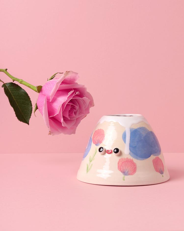 Triangular shaped creamy colored vase with pink flowers and blue clouds and a face